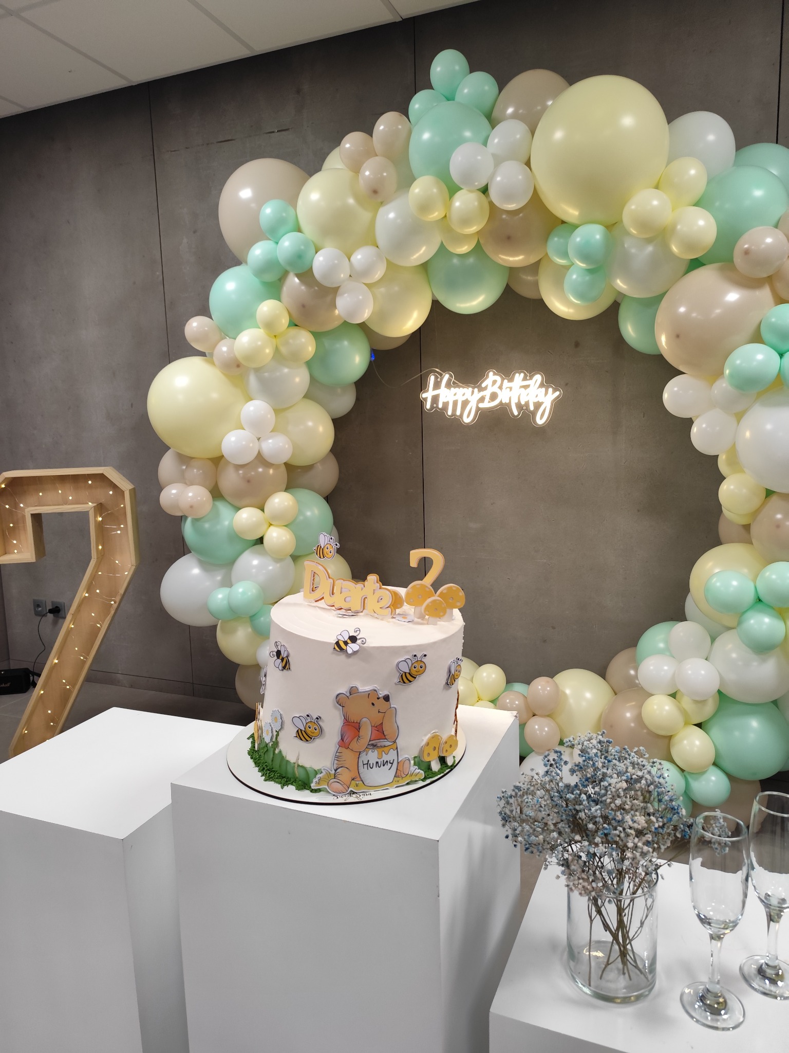 Bolo infantil com ilustrações de coelhos e um arco de balões em tons verde e creme